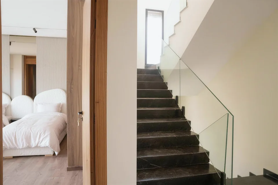 L’escalier en pierre sombre de la villa témoin, garde-corps en verre, ouvrant sur une chambre, photographié sur place.