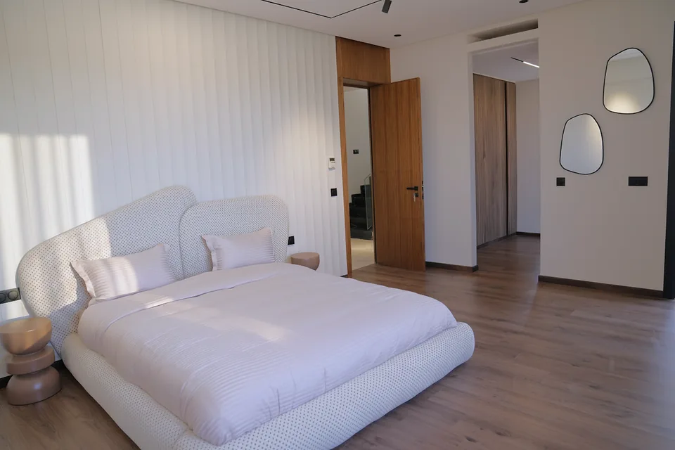 La chambre principale de la villa témoin — tête de lit capitonnée et parquet en noyer, photographiée sur place.