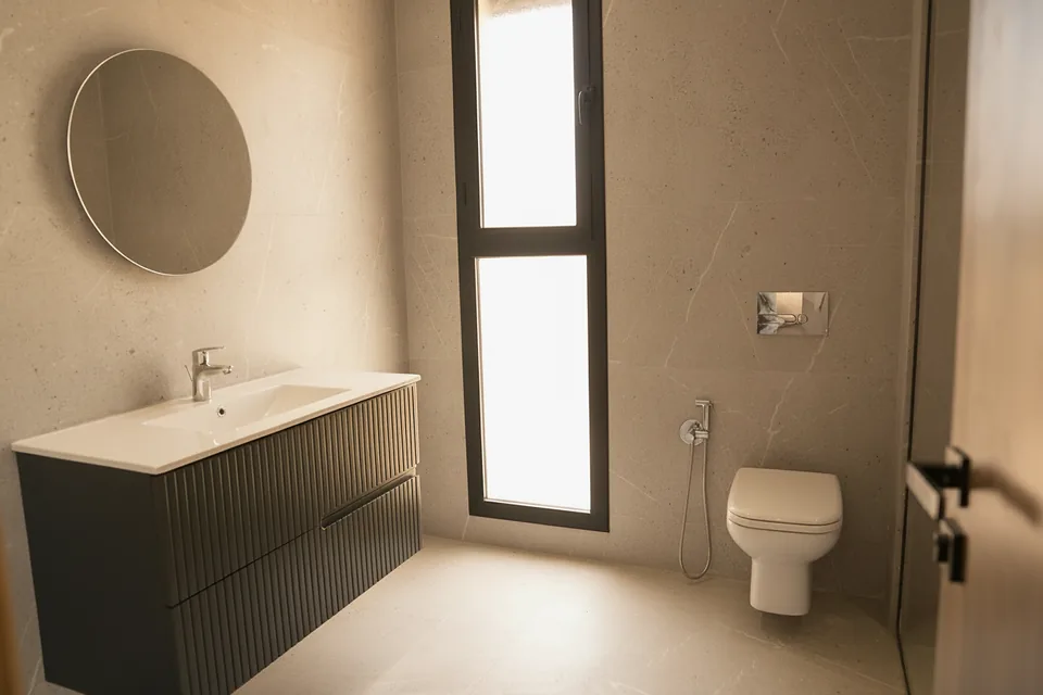 Une salle de bains de la villa témoin — pierre grand format, meuble cannelé et miroir rond, photographiée sur place.