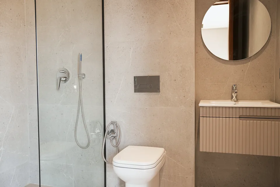 Une salle d’eau de la villa témoin — paroi de verre et pierre grand format, photographiée sur place.