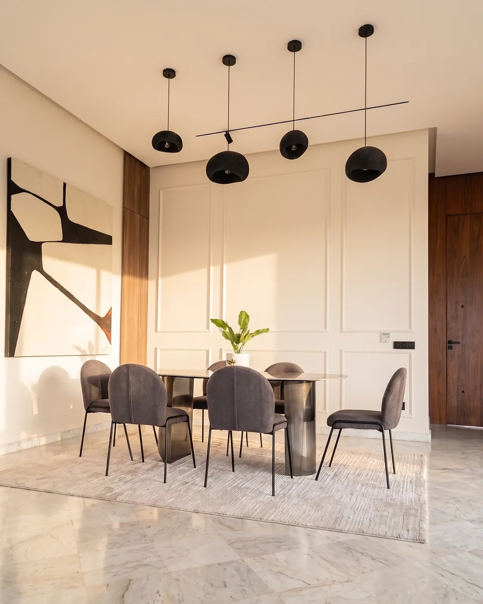 La salle à manger de la villa témoin Jnane Oum El Ghite — quatre suspensions noires au-dessus de la table, chaises en bouclé, toile abstraite et murs à moulures dans la lumière du soir, photographiée sur place.