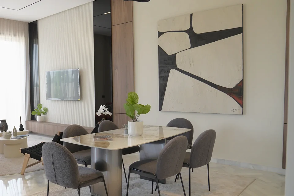 Salle à manger de la villa témoin Jnane Oum El Ghite — table en marbre, chaises rembourrées et grande toile abstraite au mur, photographiée sur place.