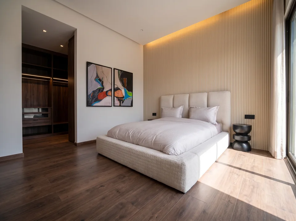 La suite parentale de la villa témoin Jnane Oum El Ghite, mur cannelé, tête de lit en bouclé, dressing en noyer et parquet.